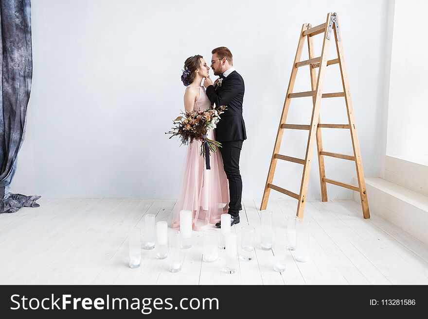 Happy bride and groom on ladder at studio. White wall background isolated