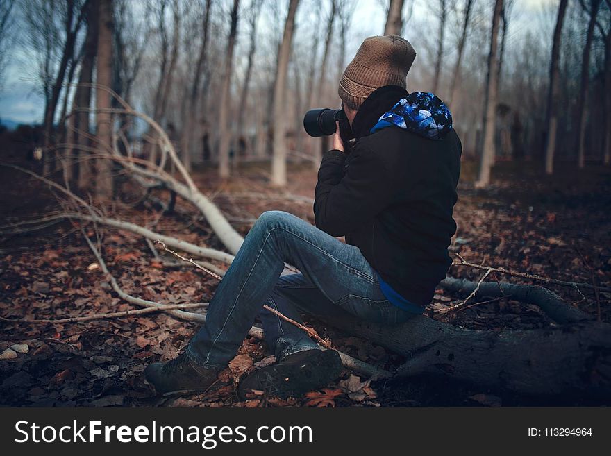 Man Wearing Black Jacket and Blue Jeans Sitting on Tree Branch