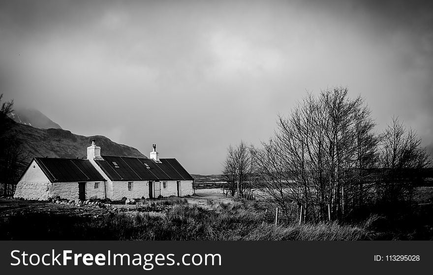 Greyscale Photo of House Within Mountain Range