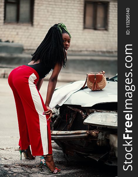 Woman in Maroon and White Pants Leaning in Front of Broken Car
