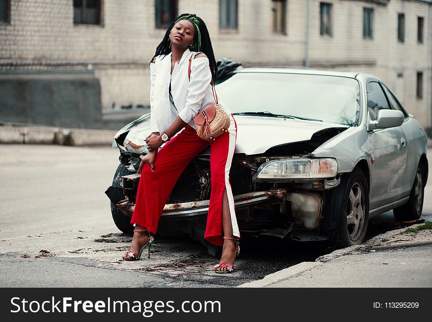 Woman in White Open Cardigan and Red and White Pants Sitting on Damage White Car