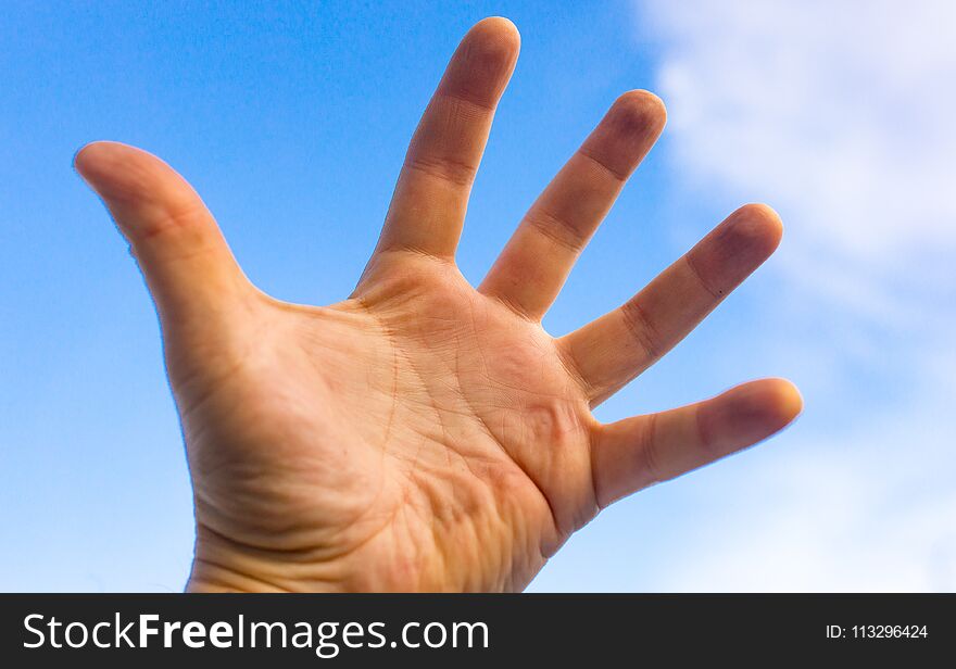 Male hand against a blue sky with clouds .