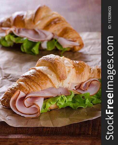 Fresh croissant sandwich with ham and salad leaf on baking paper. Fresh croissant sandwich with ham and salad leaf on baking paper