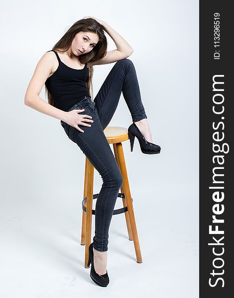 Girl with long dark hair posing on chair, black tank top jeans