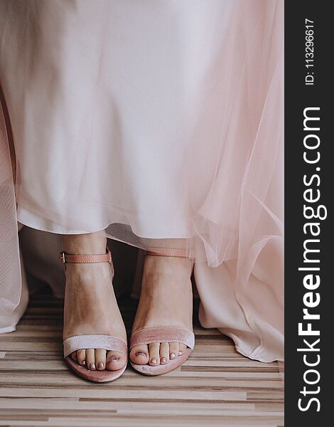 Bride`s legs close-up in velvet pink shoes and pink wedding dress transparent fabric. Vertical