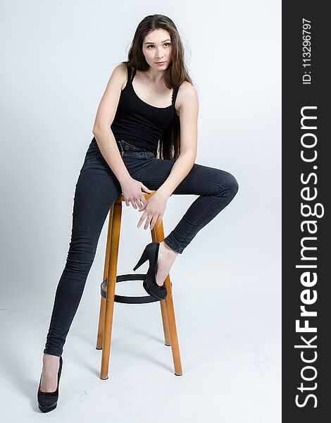 Girl with long dark hair posing on chair, black tank top jeans