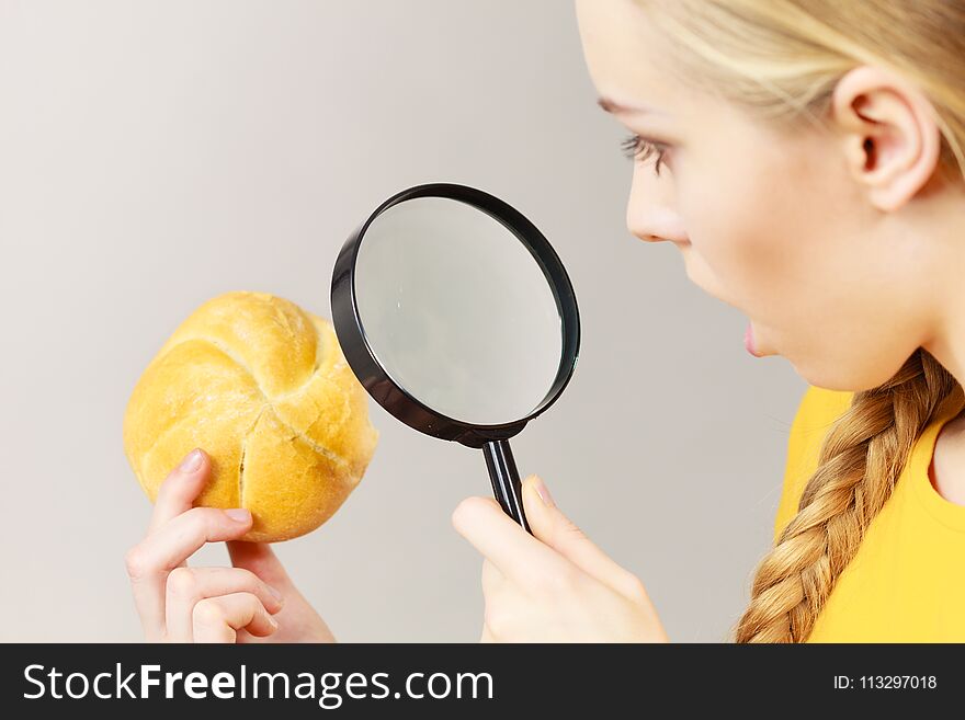 Woman holding bun bread roll and magnifying glass examine wheat product ingredients