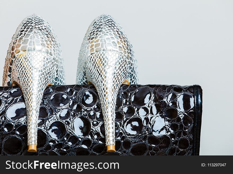 Elegant outfit, fashion concept. Black leather shiny handbag and silver high heeled shoes, closeup on gray. Studio shot. Elegant outfit, fashion concept. Black leather shiny handbag and silver high heeled shoes, closeup on gray. Studio shot.