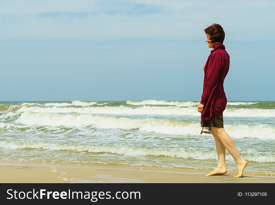 Woman having leisure time walking barefoot on beach during warm autumnal weather, shoes sandals in hand. Woman having leisure time walking barefoot on beach during warm autumnal weather, shoes sandals in hand