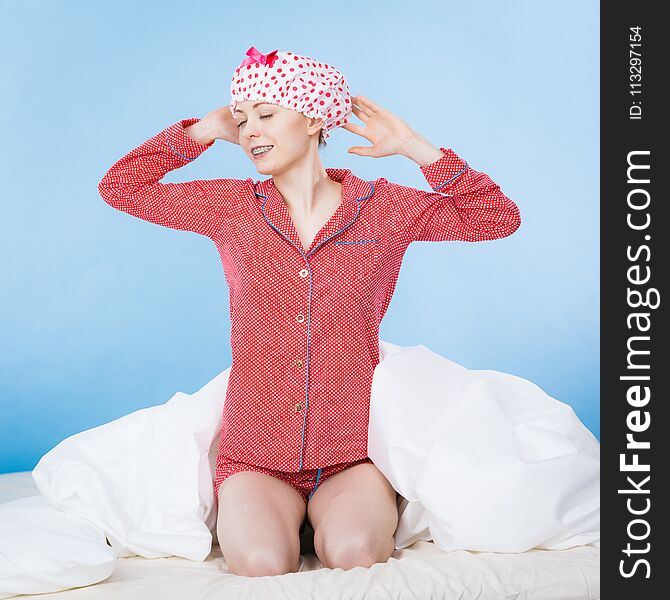 Funny happy woman after shower wearing pink pajamas and dotted bathing cap sitting on bed. Funny happy woman after shower wearing pink pajamas and dotted bathing cap sitting on bed.