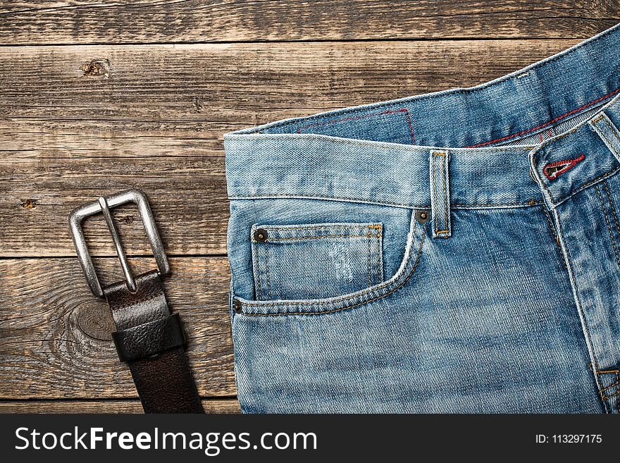 Blue Jeans and leather belt on wooden background, top view