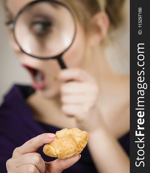 Blonde woman holding magnifying glass investigating piece of bread. Gluten products, food ingredients and pesticides concept. Blonde woman holding magnifying glass investigating piece of bread. Gluten products, food ingredients and pesticides concept.