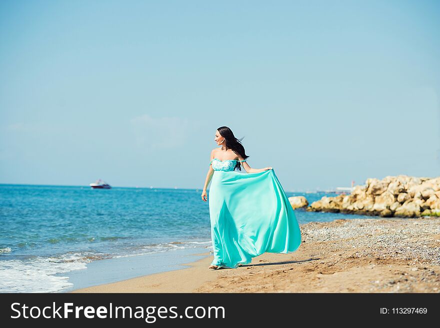 Young woman in a blue dress is walking along the beach