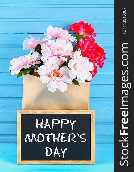 Pink peonies in a craft package with a chalkboard on a blue wooden table. Postcard for the holiday. Happy mother`s day.