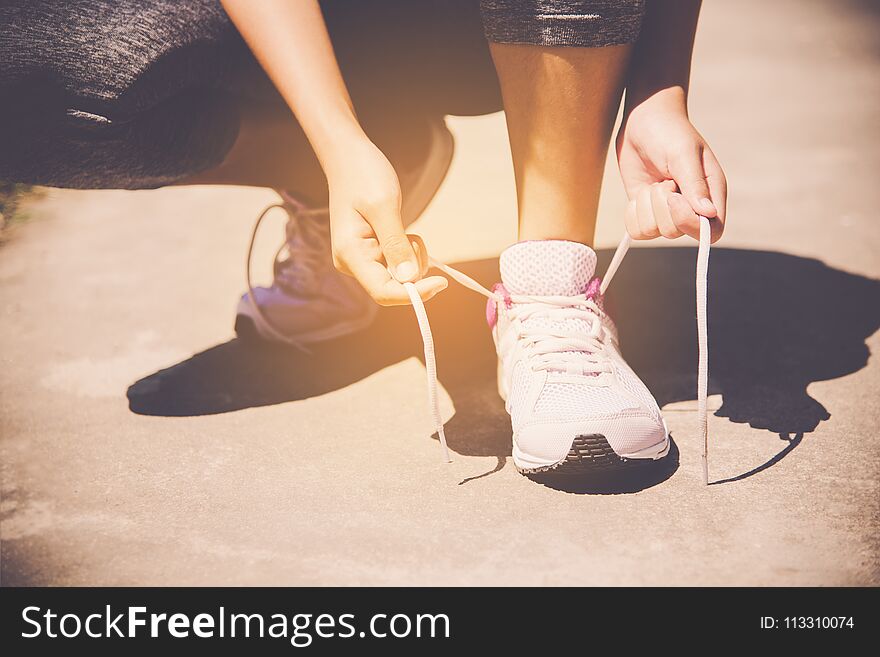 Hands of a young woman shoelace and sneakers. Shoes standing on the pavement of stones in the morning for for exercise