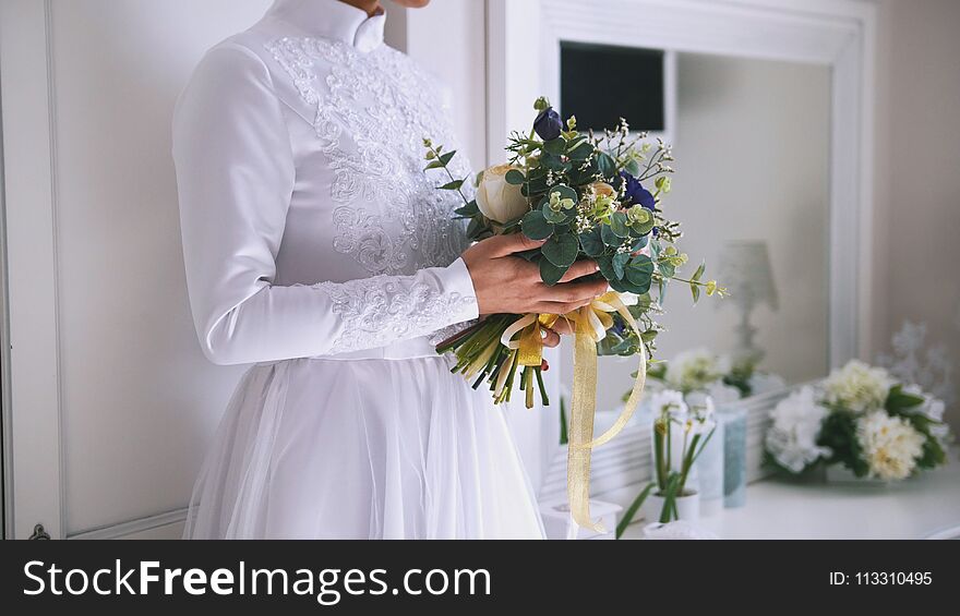 Beautiful bouquet of flowers in hands of young bride dressed in white wedding dress, close up