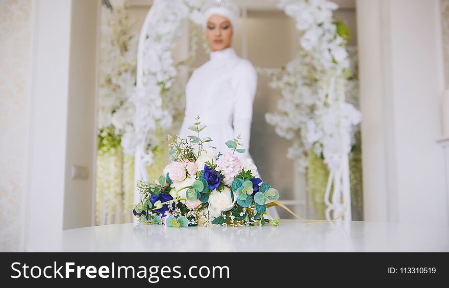 Beautiful bride in white traditional muslim dress with bunch of flowers, posing in studio