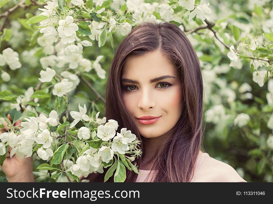 Beautiful female face closeup portrait. Pretty woman in blossom spring flowers background