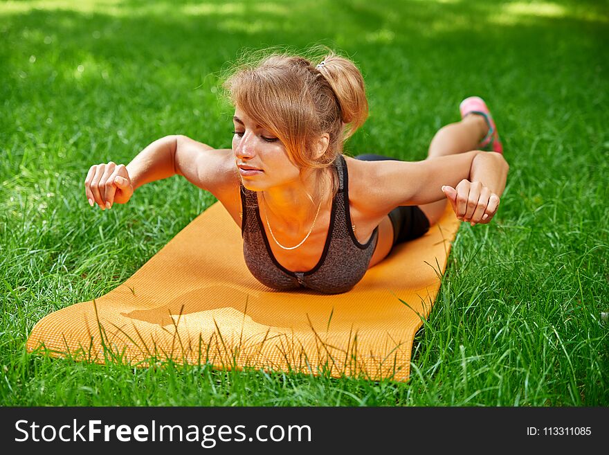 Girl doing exercises on the mat in the park on the green grass