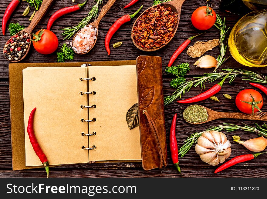 Top view open recipe book with chili peppers, garlic, oil, balsamic vinegar, salt, herbs and spices on wooden background. Cooking concept. Selective focus. Top view open recipe book with chili peppers, garlic, oil, balsamic vinegar, salt, herbs and spices on wooden background. Cooking concept. Selective focus