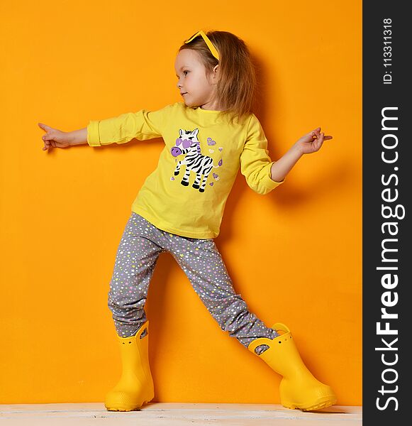 Young child baby girl kid in yellow rubber boots sunglasses and t-shirt posing on yellow