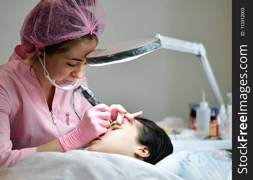 the master does the tattoo on the eyebrows to the girl. the master does the tattoo on the eyebrows to the girl.