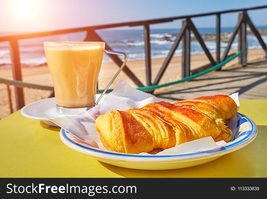 Coffee Cup With Croissant On Table In Cafe Terrace And View On The Sea With Waves