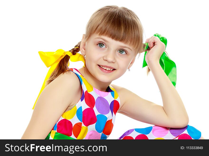 A beautiful Caucasian little blonde girl with long pigtails, in which large colored bows are braided, and a short bangs on her head. In a short summer dress, a pattern of multi-colored circles. A beautiful Caucasian little blonde girl with long pigtails, in which large colored bows are braided, and a short bangs on her head. In a short summer dress, a pattern of multi-colored circles.