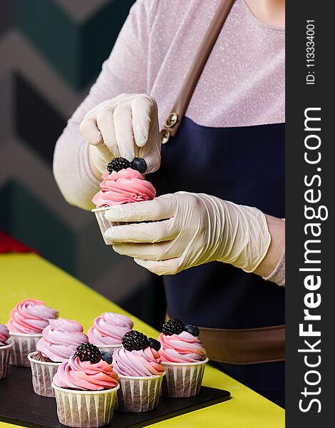 Woman decorating cupcakes with berry on the table in kitchen