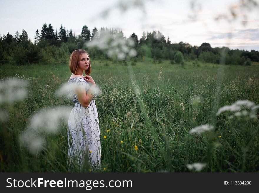 Beautiful brunette in the evening summer field with bouquet of meadow flowers