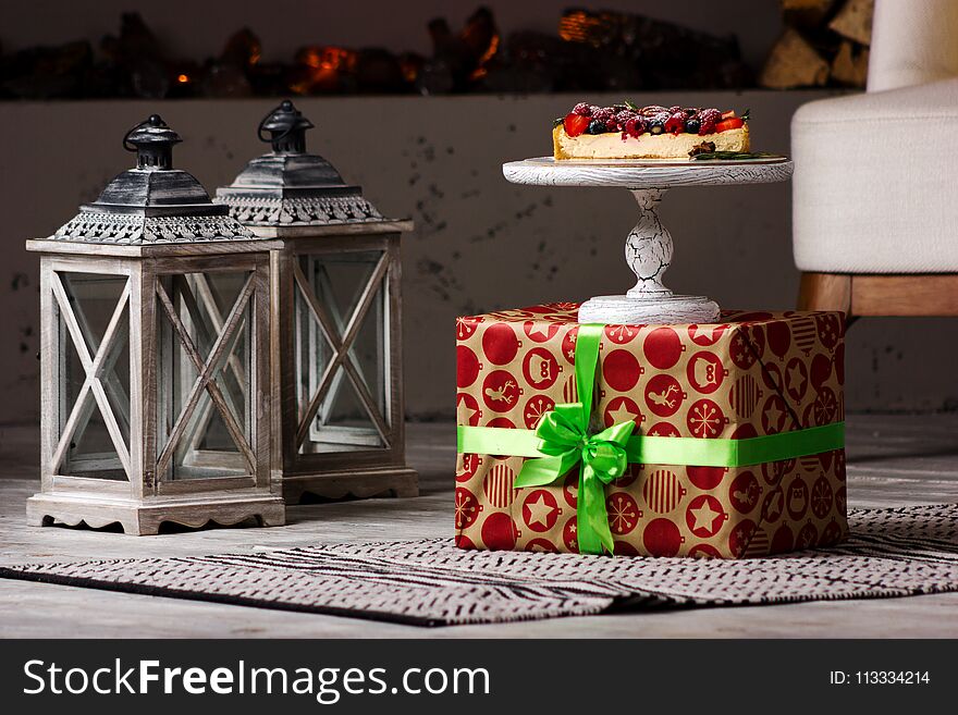 Delicious cheesecake section with different berry on the present box with gray lanterns on the floor. Delicious cheesecake section with different berry on the present box with gray lanterns on the floor
