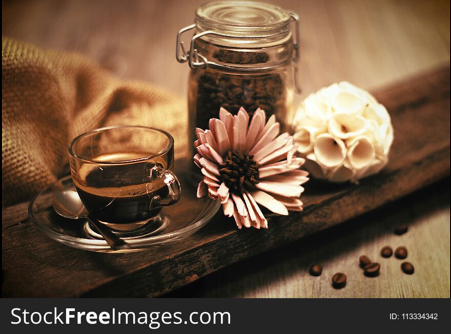 Lovely composition with a cup of coffee and coffee beans and a flower on a wooden table