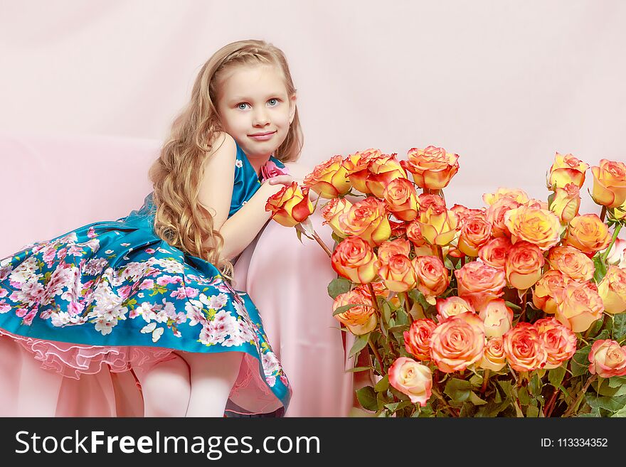 A beautiful little girl with long, light, curly hair, in a blue long skirt. She sits on a pink couch beside a large bouquet of tea roses. A beautiful little girl with long, light, curly hair, in a blue long skirt. She sits on a pink couch beside a large bouquet of tea roses.