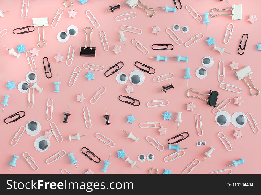 Beautiful pink background with stationery. Staples, office buttons and asterisks are in disarray. In the center is a