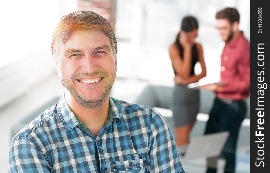 Handsome businessman is looking at camera and smiling while standing with crossed arms in office, his colleagues are working in the background. Handsome businessman is looking at camera and smiling while standing with crossed arms in office, his colleagues are working in the background