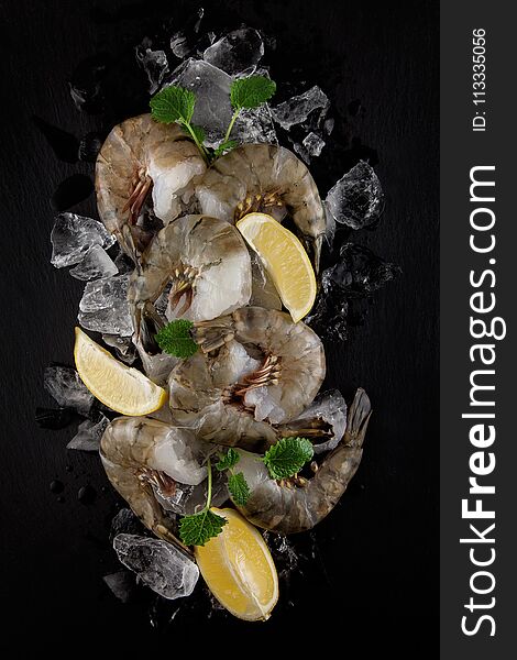 Fresh raw king prawns with lemon and lemon balm on dark slate kitchen plate