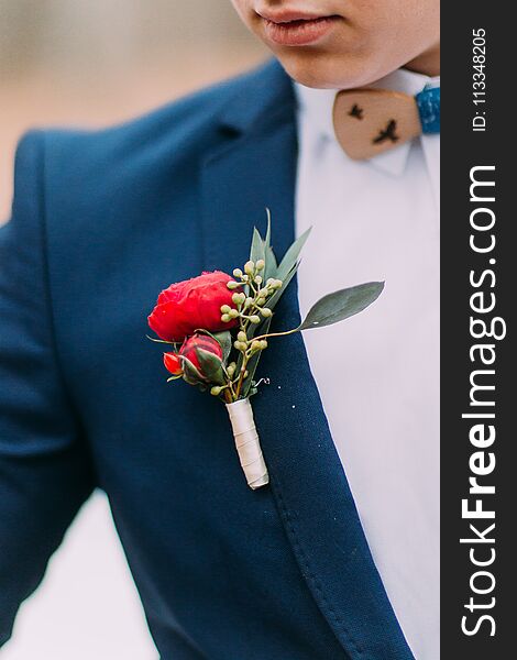 Red boutonniere in the grooms jacket close up.