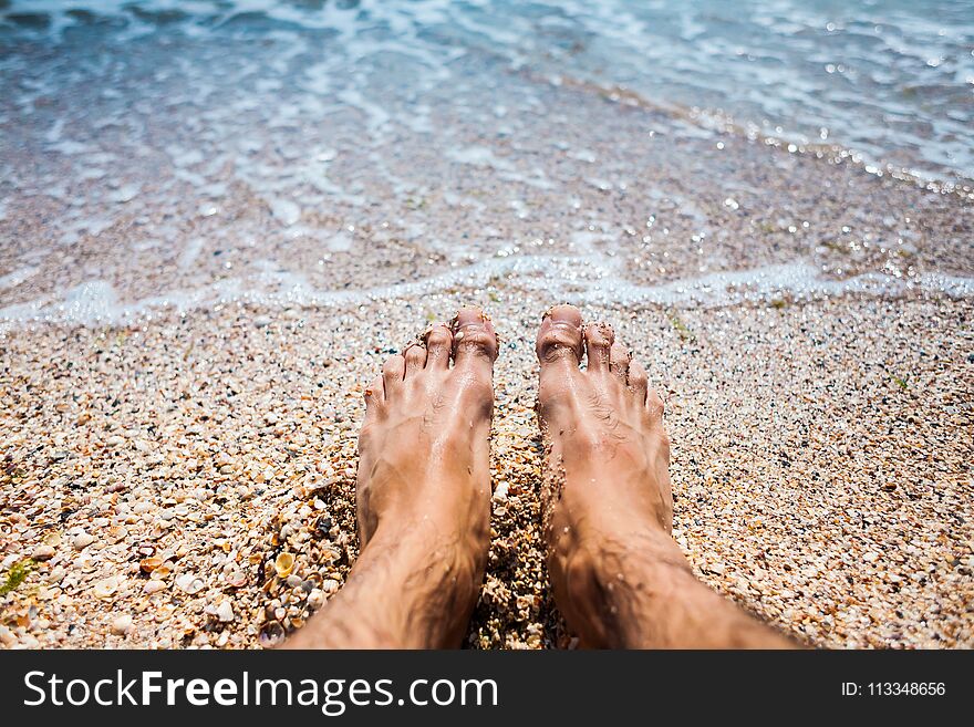 Feet in the sea water. Men`s feet on the sandy shore. Selfy near the ocean shore.