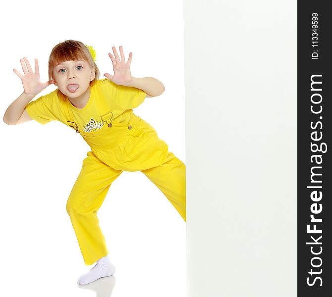 Girl with a short bangs on her head and bright yellow overalls.She crouched down on the white advertising banner.