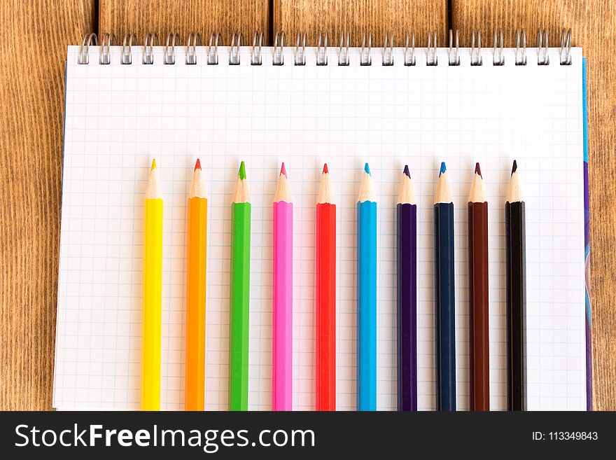 Set of colored pencils on school notebook on wooden background .