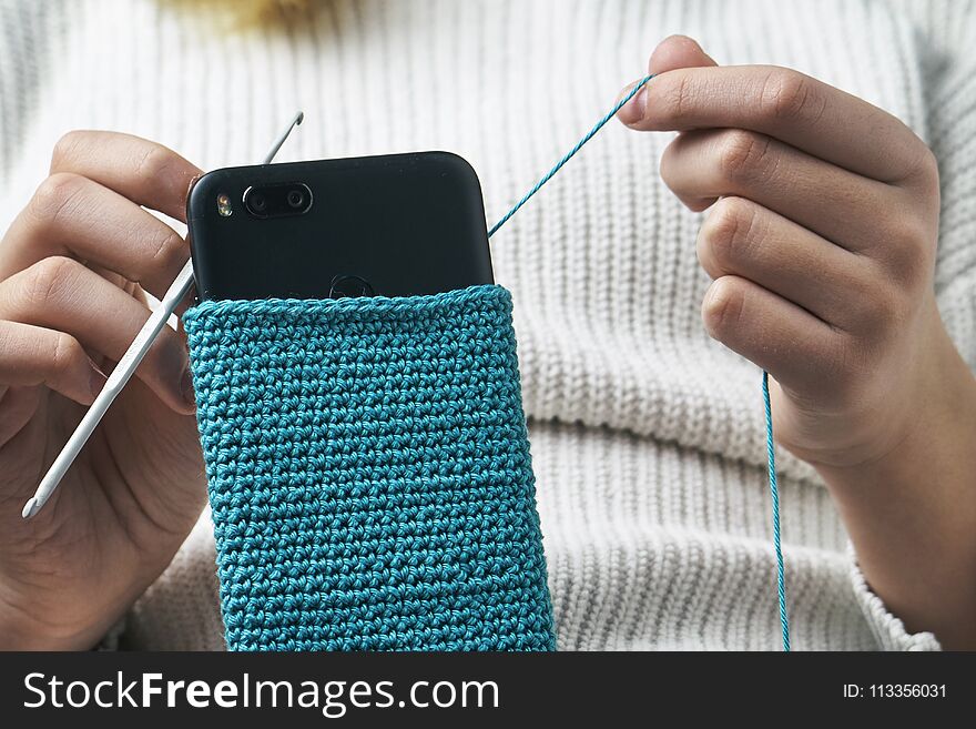 Teen girl crocheting a woolen case for a smartphone. Teen girl crocheting a woolen case for a smartphone