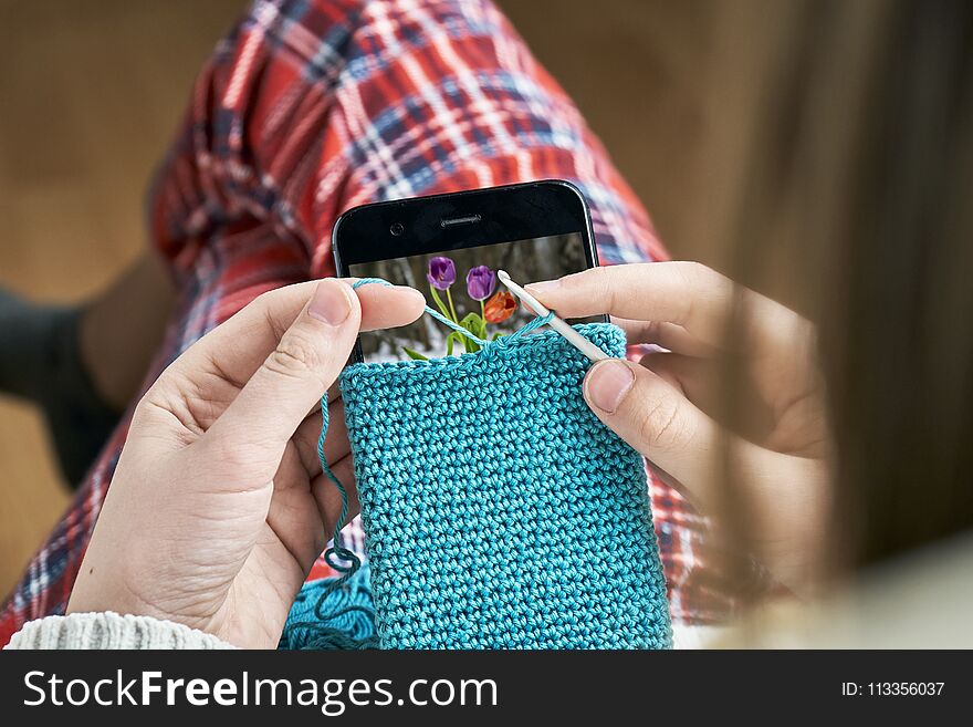 Girl crocheting a woolen case for a smartphone with white screen. Girl crocheting a woolen case for a smartphone with white screen