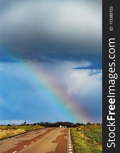 Beautiful colorful rainbow at the end of asphalt road, perspective view, France