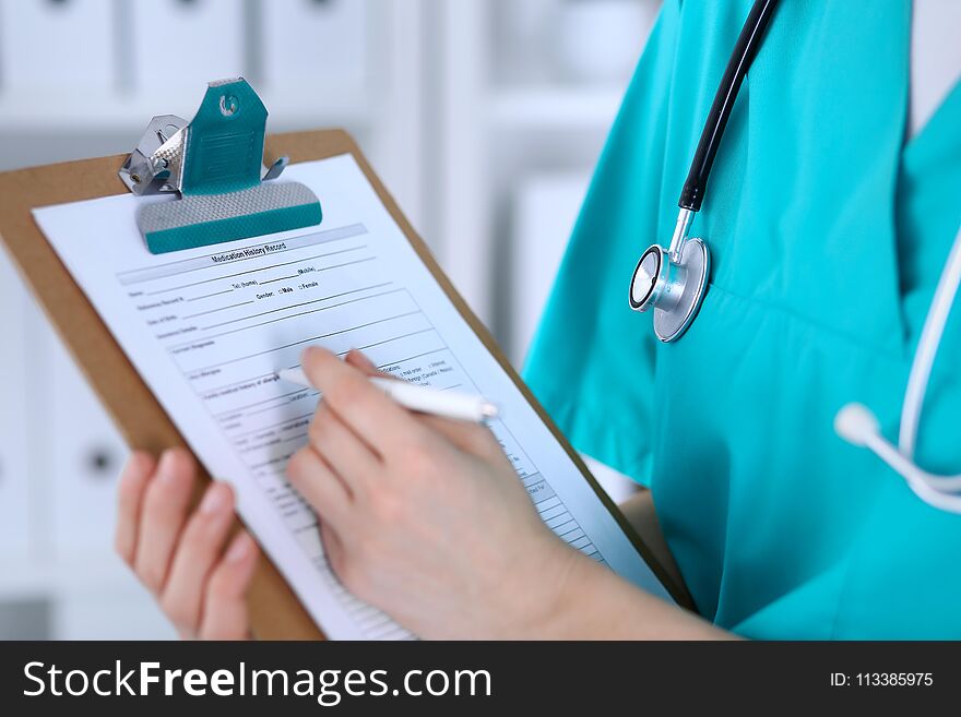 Female doctor filling up medical form on clipboard closeup. Physician finish up examining his patient in hospital and ready to give a prescription to help. Healthcare, insurance and medicine concept.