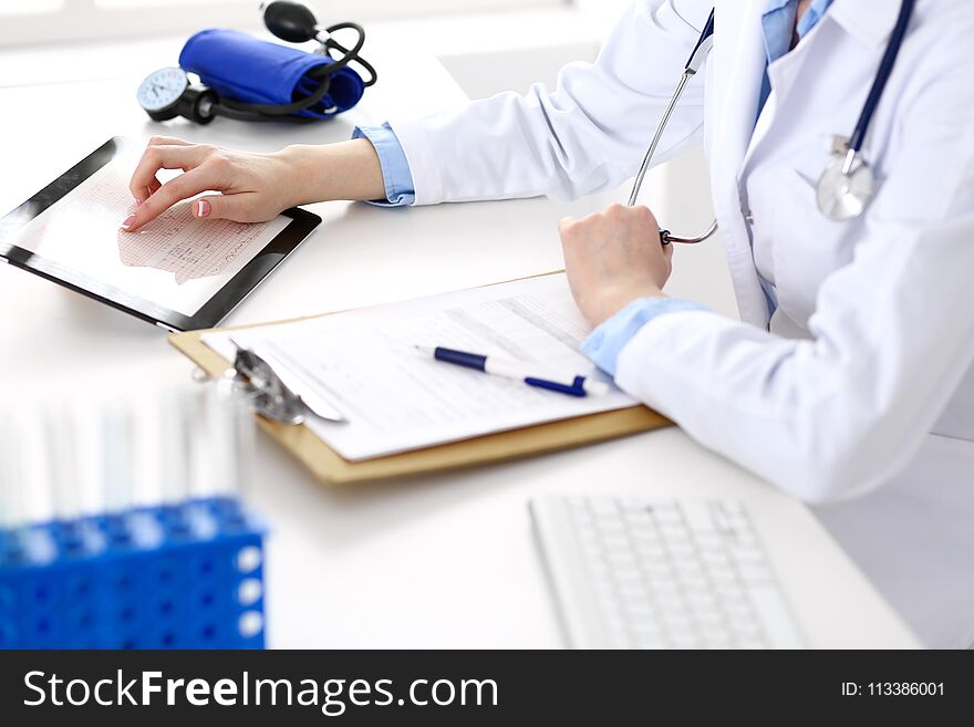 Woman doctor using tablet computer while sitting at the desk in hospital closeup. Cardiologist checks heart diagrams with tablet pc. Healthcare, insurance and smart technology in medicine concept.