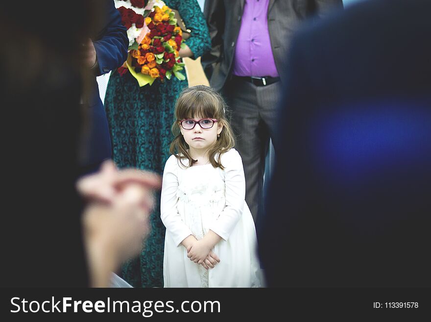 Sad little girl in white dress in the crowd at the wedding.