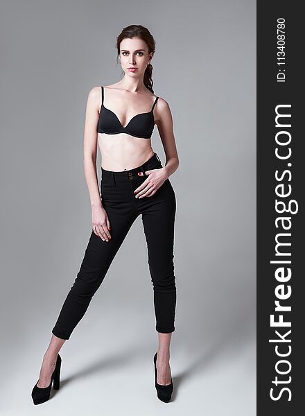 Studio fashion shot: portrait of attractive young woman in pants and bra. Full length