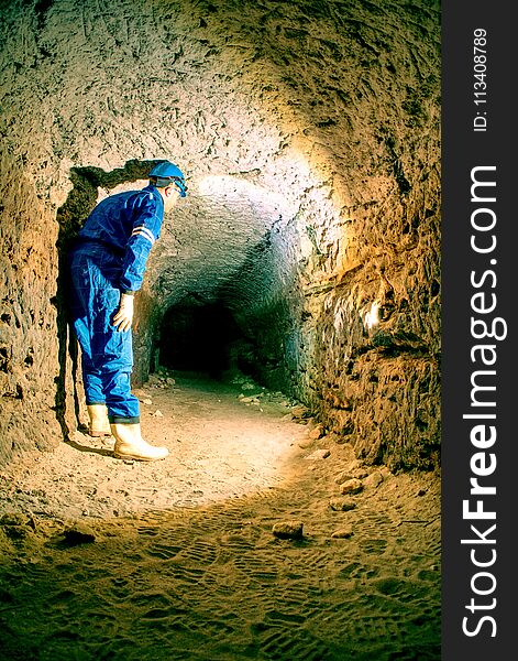 Workerman with helmet and protective suit using glowes and head lamp. Man do job in old mine ventilation shaft. Underground worker. Workerman with helmet and protective suit using glowes and head lamp. Man do job in old mine ventilation shaft. Underground worker.