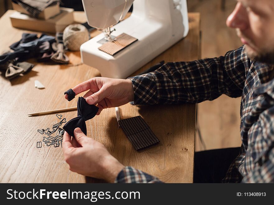 Good looking young man working as a tailor and using a sewing machine in a textile studio. makes bow ties butterflies. Good looking young man working as a tailor and using a sewing machine in a textile studio. makes bow ties butterflies