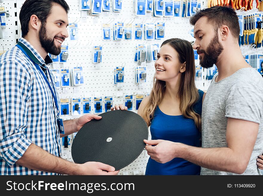 Salesman in checkered shirt is showing couple of clients new grinding wheel in power tools store. Salesman in checkered shirt is showing couple of clients new grinding wheel in power tools store.